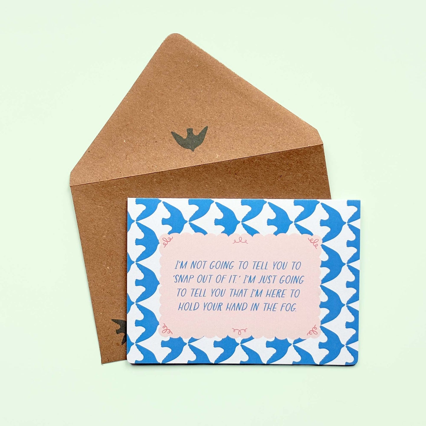 Card with blue bird pattern and pink text on a light green background, accompanied by a Kraft brown envelope. The text on the card reads: "I'm not going to tell you to 'Snap out of it. I'm just going to tell you that I'm here to hold your hand in the fog.'"