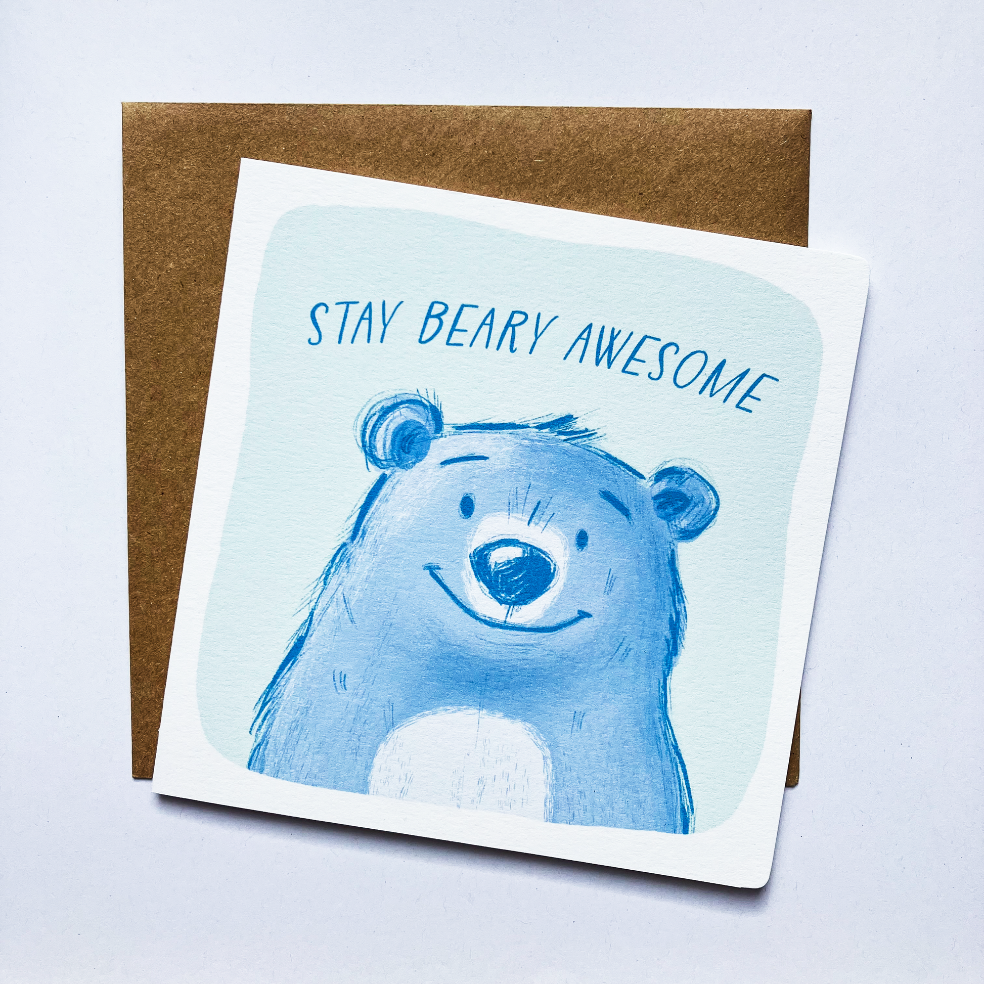 A square birthday card with a blue bear illustration and the text 'Stay Bear-y Awesome' on it, placed on a kraft brown envelope