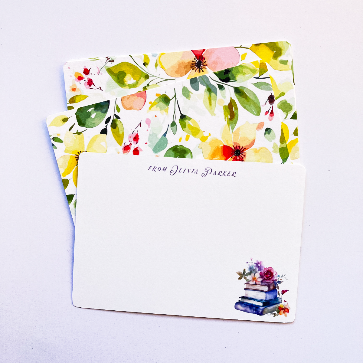 Personalised flat notecard featuring a watercolour stack of books and flowers, layered in front of matching bright yellow and green floral pattern cards.