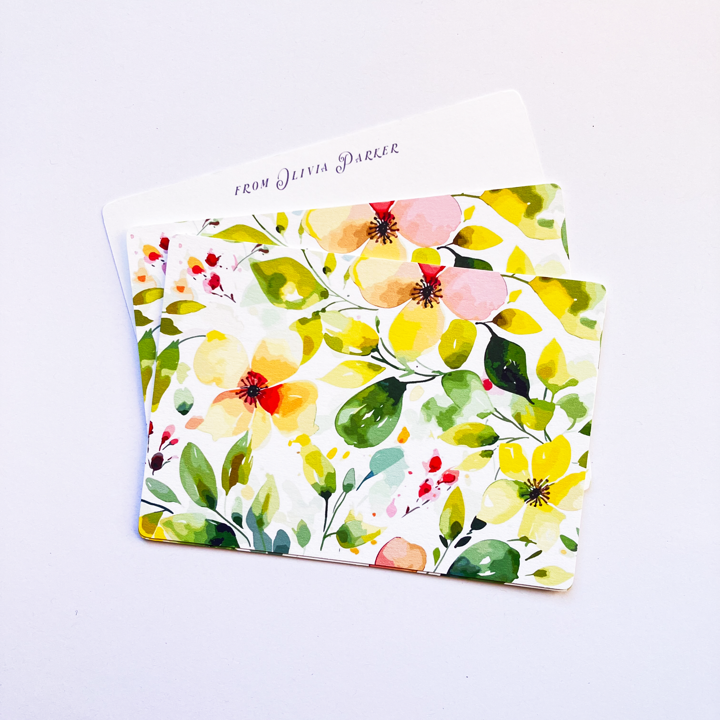 Vibrant yellow and green watercolour floral pattern backing for bespoke stationery, with a personalised "From Olivia Parker" note card partially visible behind it.