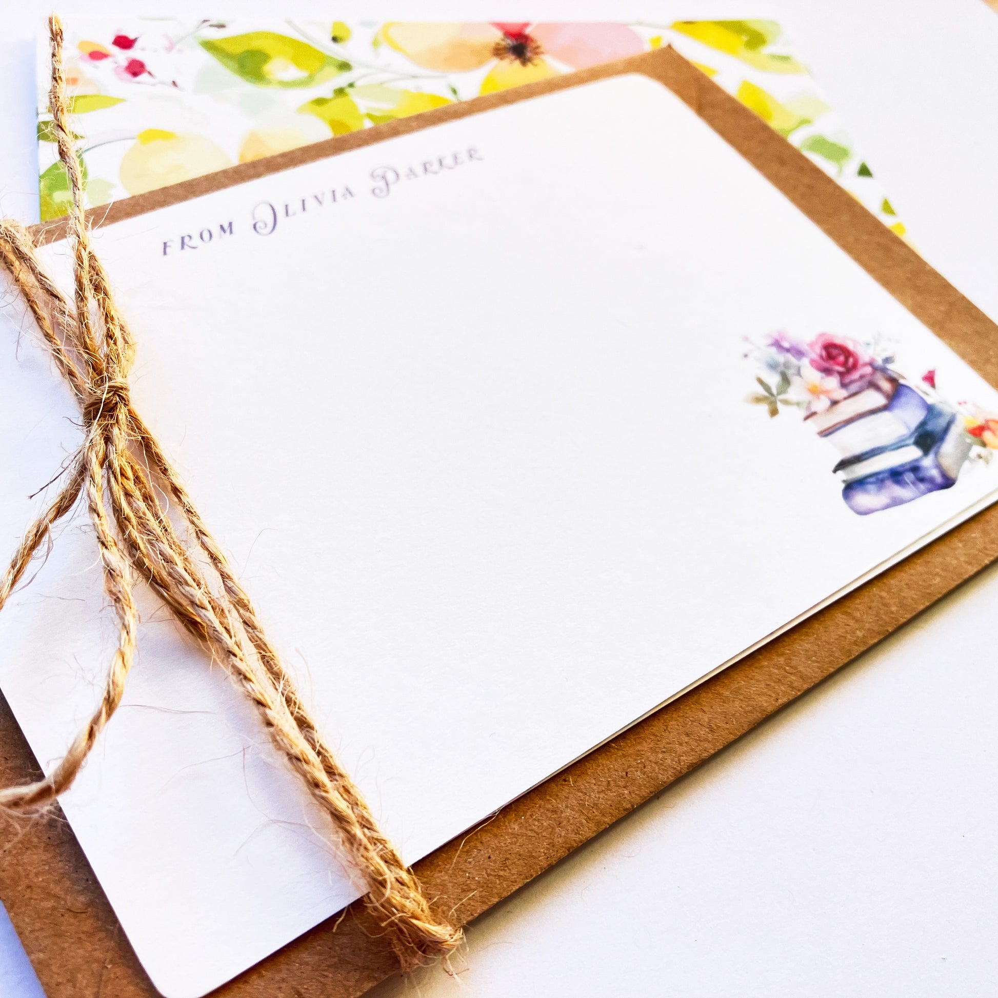 Bespoke book lover note card tied with rustic jute twine over a kraft envelope, featuring personalised text and a watercolour illustration of stacked books with flowers.