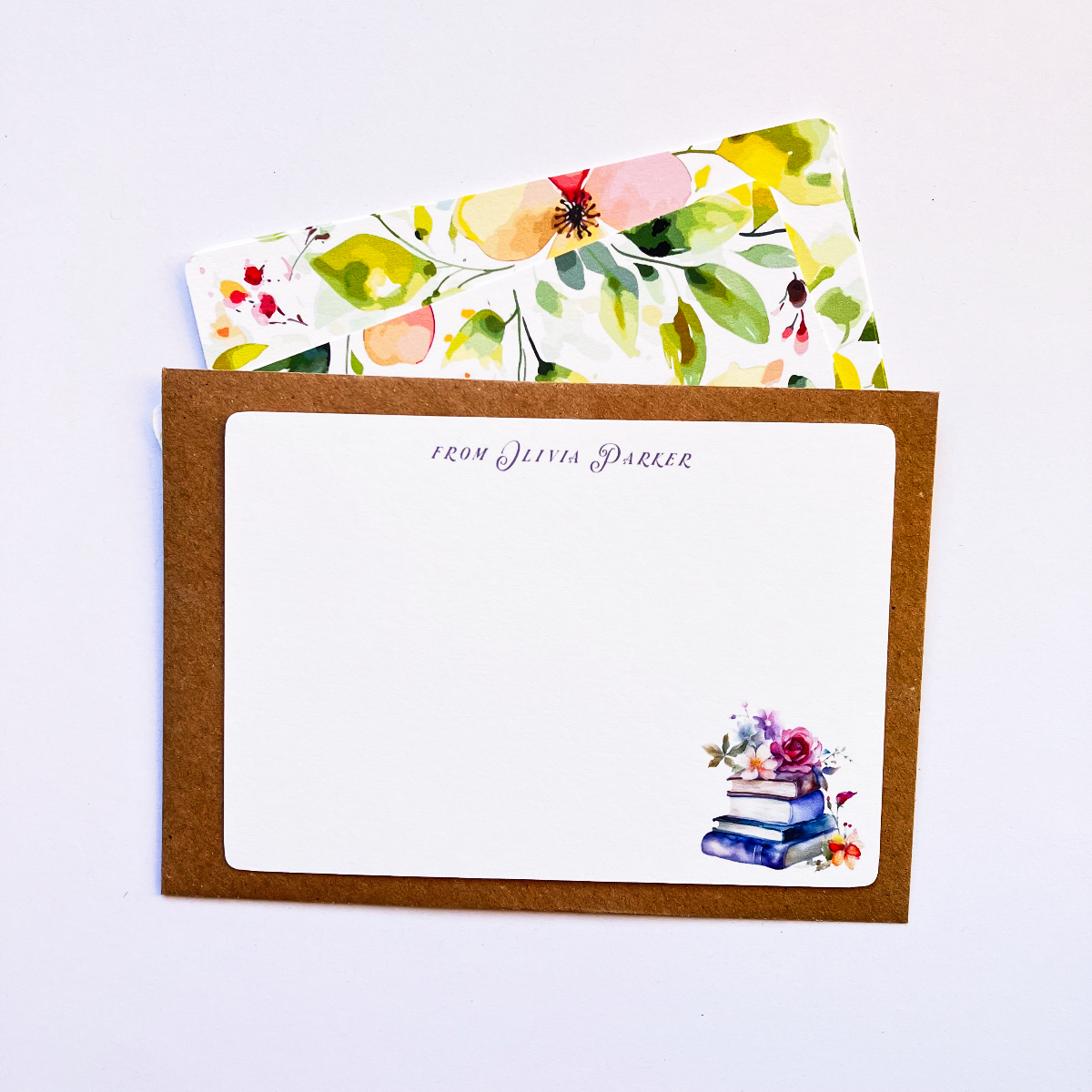 Bespoke notecard with floral book art and personalised text, displayed on a closed kraft envelope with vibrant yellow watercolour floral cards behind it.